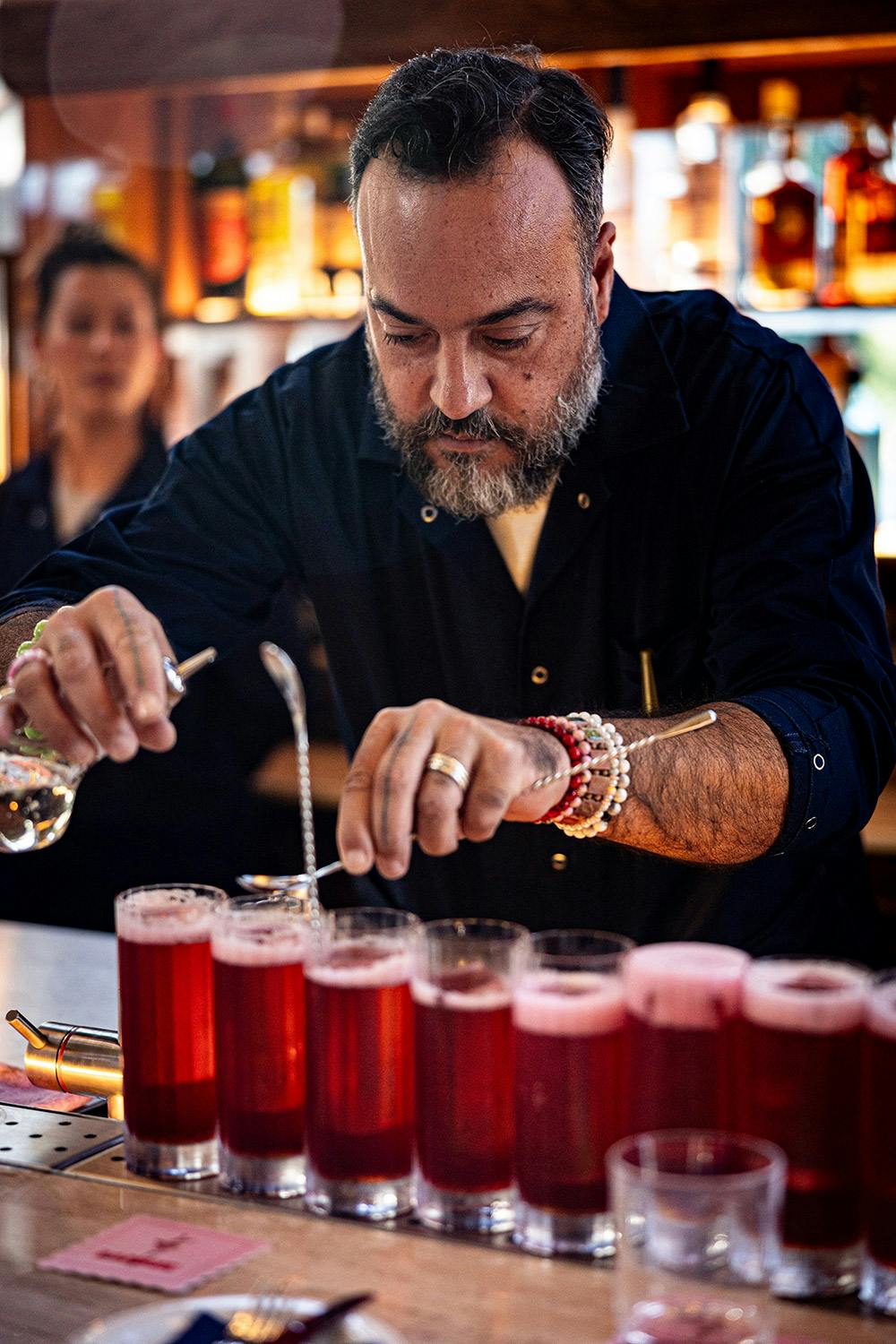 An expert bartender serves a row of red cocktails
